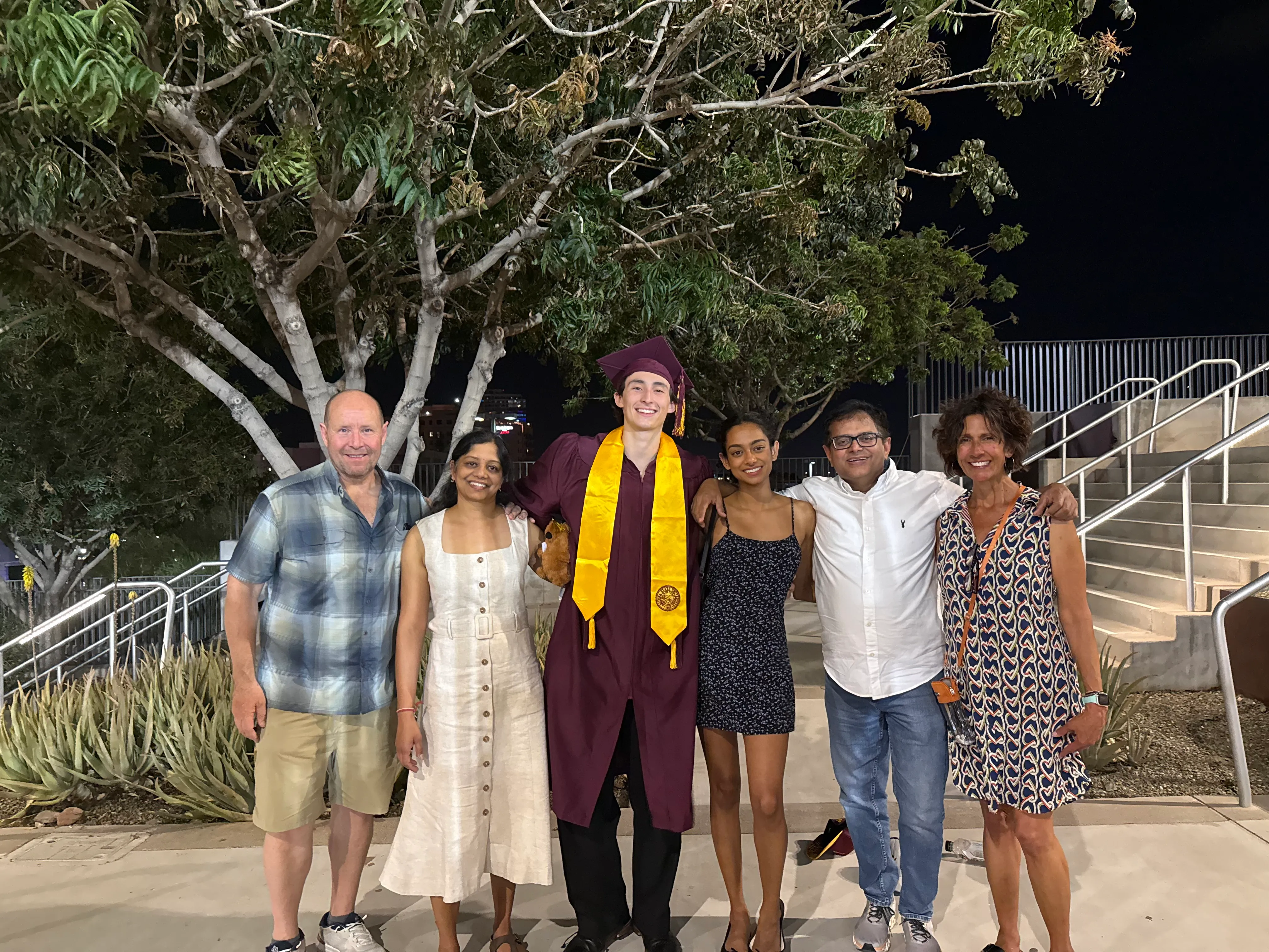 Jackson in a maroon cap and gown with a gold stole, standing with five family members under a tree at night after the Arizona State ceremony