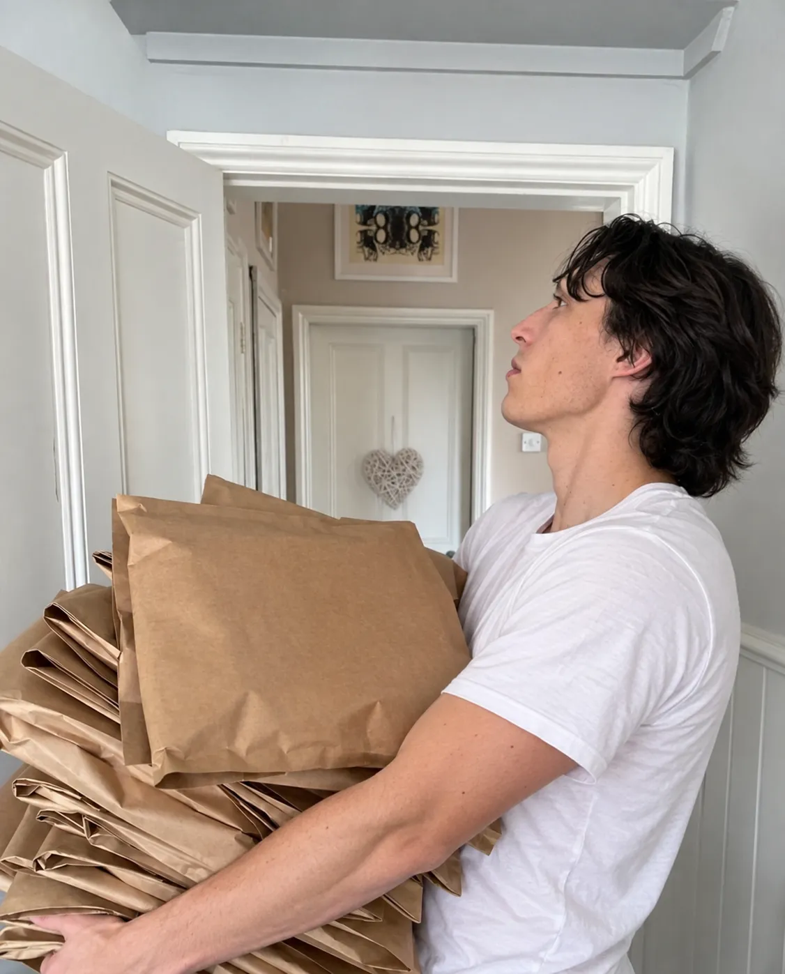 Jackson carrying a stack of kraft paper mailers down a hallway, an order ready to ship